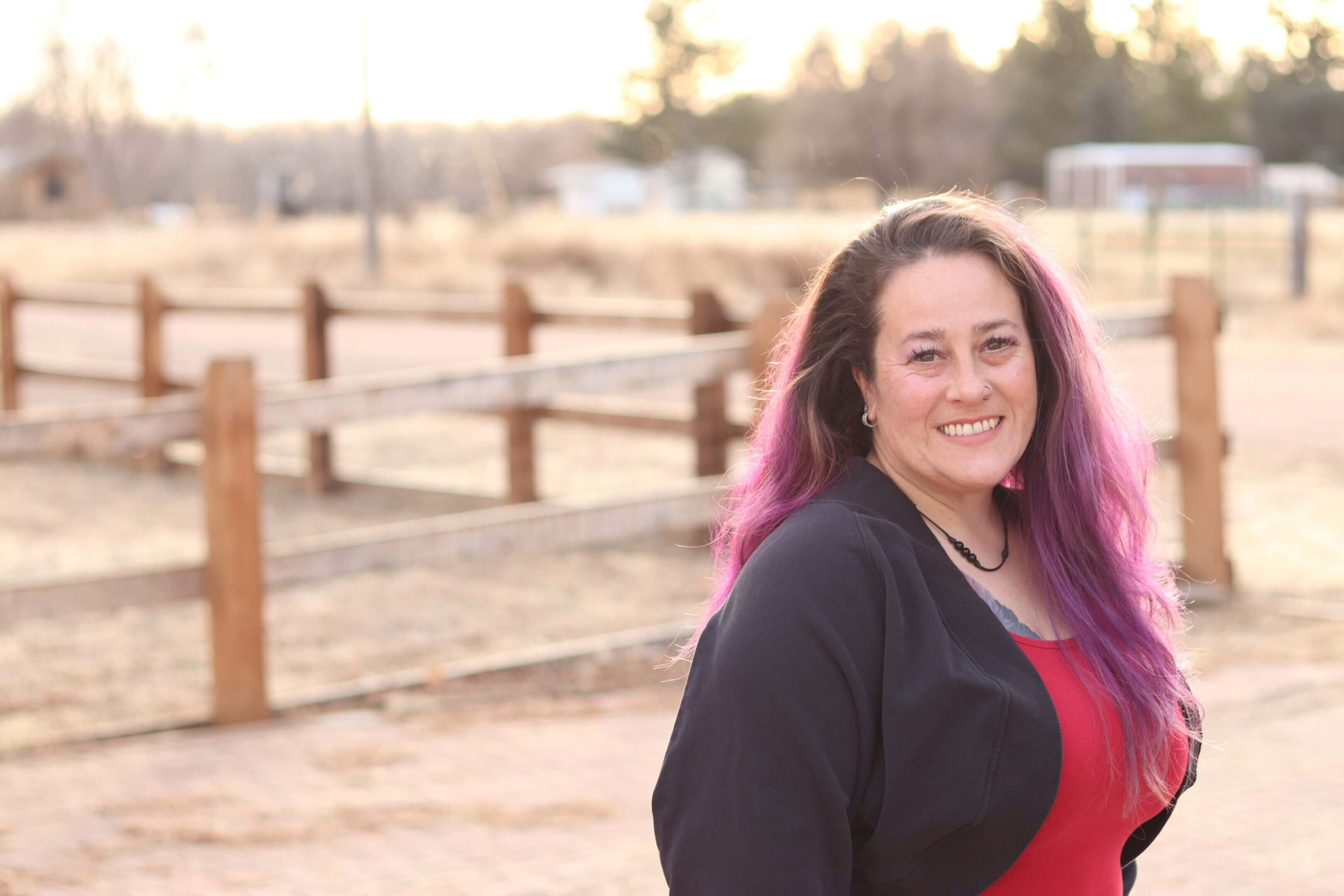 Smiling woman with pink hair outdoors.