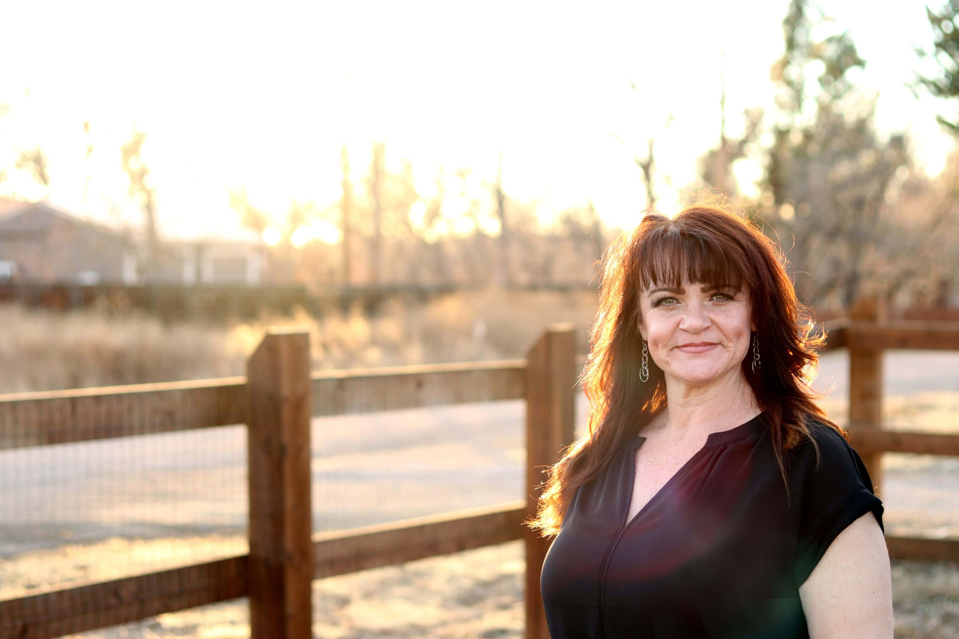 Woman standing outdoors near wooden fence.